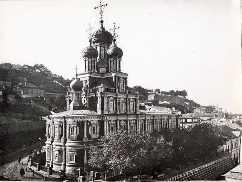 Черно-белая фотография Строгановской церкви в Нижнем Новгороде, снятая со стороны склона, с видом на историческую застройку города.